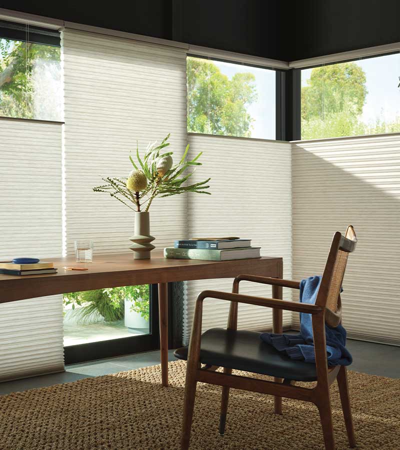 Top-down, bottom-up honeycomb shades in a home office, lowered from the top with the same fabric all the way down and a view of green trees above the desk