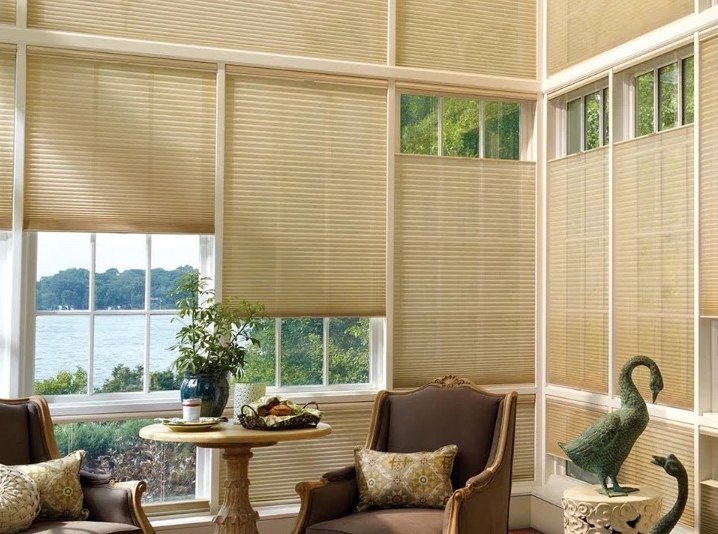 A sunroom with tan honeycomb shades set at different heights, some lowered from the top to let daylight in above and some raised from the bottom, with a lake view