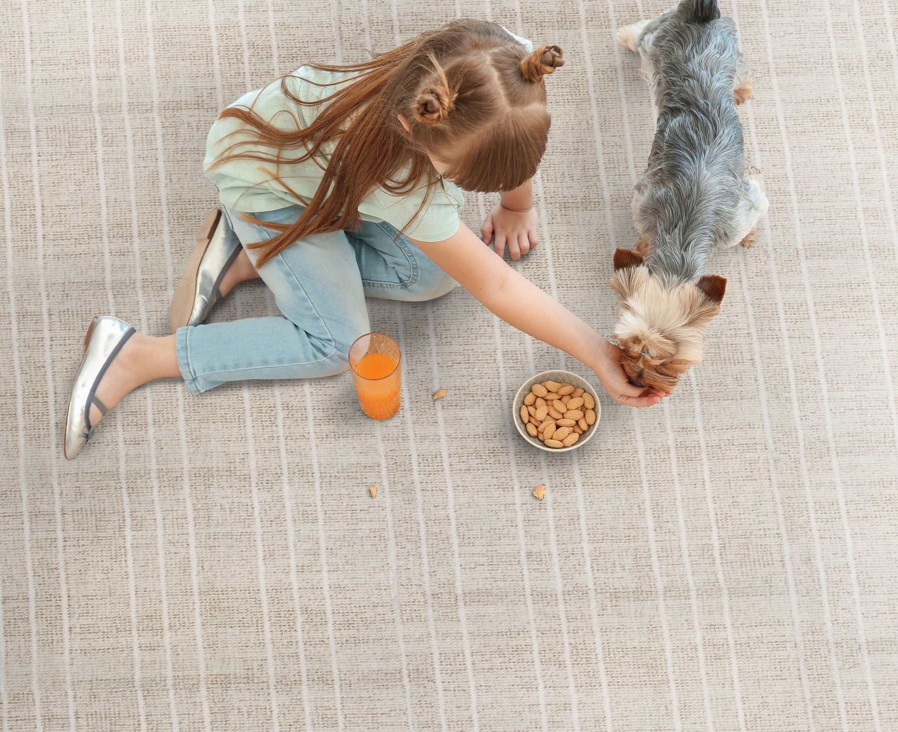 A girl feeding a small dog on San Martino carpet, with a glass of juice beside her