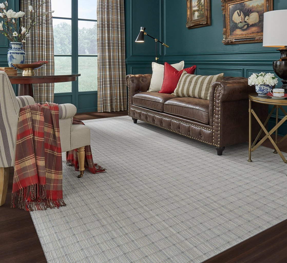 Whitaker wool carpet made into an area rug on a dark wood floor, under a brown leather sofa in a living room with deep teal walls